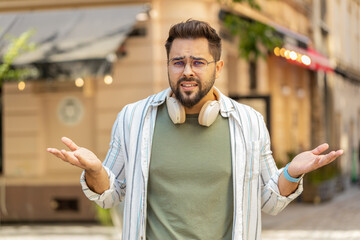 Doubtful sad frustrated young man tourist shrugging shoulders dont know answer incertitude gesture...