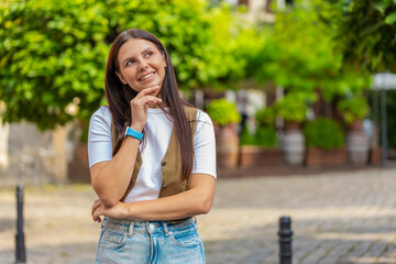 Thoughtful smiling happy brunette young woman in with pensive expression, pondering a solution, doubting question, thinking inspiration dreaming outdoors. Adult girl standing on urban city street.