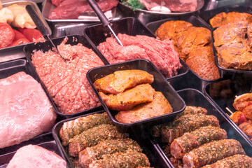 variety of raw meat and marinated cuts displayed in butcher shop counter