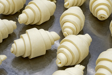 Group of raw uncooked croissants on a metal tray, ready to be baked