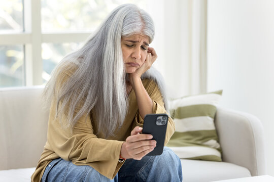 Unhappy frustrated senior Hispanic woman reading message on smartphone