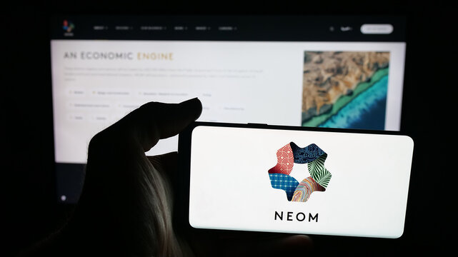 Stuttgart, Germany - 09-29-2025: Person holding mobile phone with logo of Saudi Arabian real estate project NEOM on screen in front of web page. Focus on phone display.