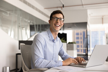 Cheerful handsome young business leader man typing on laptop