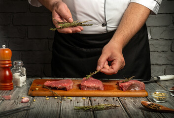 A chef is seasoning fresh beef steaks with herbs in a rustic kitchen. The wooden cutting board holds the meat, while spices and seasonings surround the scene, highlighting culinary preparation