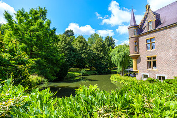 Wooded landscape surrounding moat of TerWorm Castle, red brick walls, side tower and windows, green leafy trees in background, sunny spring day in Heerlen, South Limburg, Netherlands