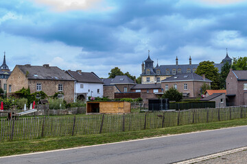 Landscape of gardens, farm orchards, country road and village brick houses with gray roof of castle in background against stormy sky, cloudy day on outskirts of Oud-Rekem, Limburg, Belgium