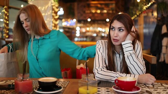 Upset young woman crying at a cafe table while her attentive friend provides comfort and emotional support during a difficult time, holding her shoulder and offering a tissue