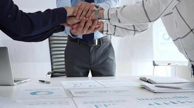 Teamwork and business collaboration with colleagues joining hands over financial charts, symbolizing unity, partnership, success, and strategic corporate planning