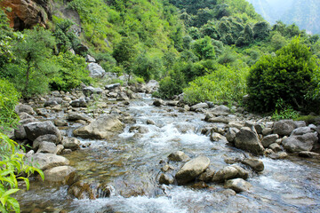 A clear mountain stream rapidly flowing over and around numerous smooth, gray boulders and rocks,...