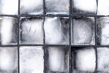 Close-up of clear ice cubes neatly arranged in a tray with a glossy finish, showcasing their transparency, texture, and reflections. Ideal for food or drink-related projects.