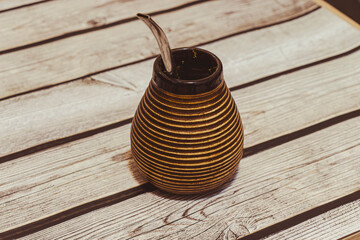 A modern striped gourd mate container placed on a rustic wooden table. The vessel, often used for traditional South American tea, showcases beautiful craftsmanship and design.