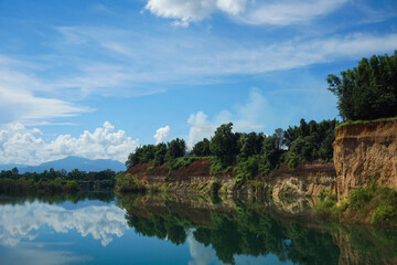 Grand Canyon of Thailand in Chiang Mai, a stunning natural landmark featuring high, orange-hued earthen cliffs topped with lush green forest, perfectly mirrored in the tranquil, blue water below