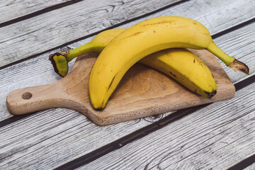 Three ripe bananas arranged on a wooden cutting board. The yellow color contrasts with the rustic wooden surface, ideal for food-related designs and culinary content.