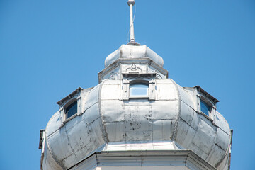 The ornate metal tower of a historic European building with small windows, set against a clear blue...