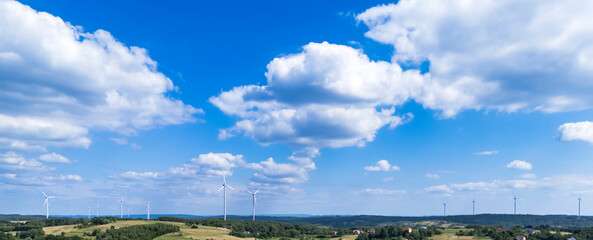 A panoramic view of a wind farm on rolling green hills under a bright blue sky. Wind turbines are visible, showcasing renewable energy and a sustainable future in nature.