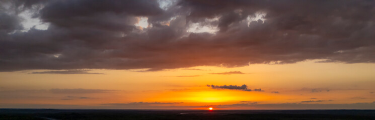 Stunning sunset view over the horizon with vibrant orange and yellow hues painted across the sky. Clouds add depth and intrigue to this serene landscape.