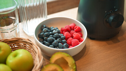 Healthy lifestyle setup in the kitchen. Fresh fruits apples, blueberries, raspberries, and avocado arranged beside a blender, prepared for making a homemade smoothie