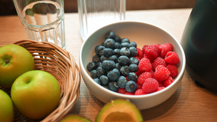 Healthy lifestyle setup in the kitchen. Fresh fruits apples, blueberries, raspberries, and avocado arranged beside a blender, prepared for making a homemade smoothie