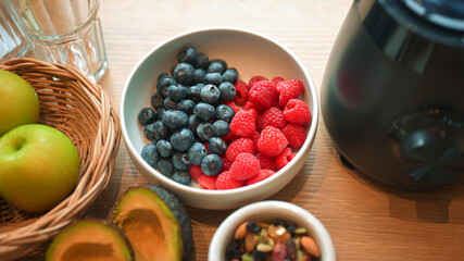 Healthy lifestyle setup in the kitchen. Fresh fruits apples, blueberries, raspberries, and avocado arranged beside a blender, prepared for making a homemade smoothie