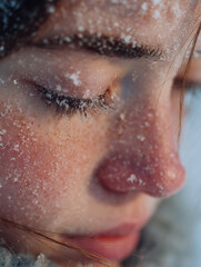 Fototapeta premium A young woman stands in a tranquil snowy landscape, illuminated by the gentle soft glow of winter. Delicate snowflakes gracefully fall, landing on her eyelashes, creating a serene moment on this peace