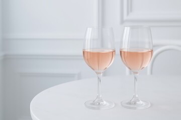 Fototapeta premium Two glasses of delicate French rosé wine on a white table, captured in soft natural light with minimalist elegance.