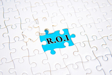 Fototapeta premium White puzzle pieces with one missing piece revealing the word ROI on blue background. Concept of business strategy, investment return, analysis, and financial performance improvement.