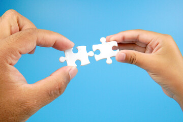 Two hands holding puzzle pieces facing each other on blue background. Concept of teamwork, partnership, connection, collaboration, unity, and problem solving in business or relationship.