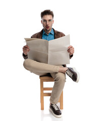 surprised young man with glasses reading newspaper and being shocked