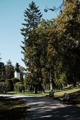 Peaceful park alley with benches, trees, and a monument on a sunny day in Belgrade, Serbia.