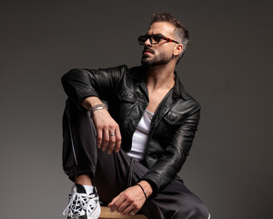confident cool man with sunglasses looking to side and sitting with elbow on knee