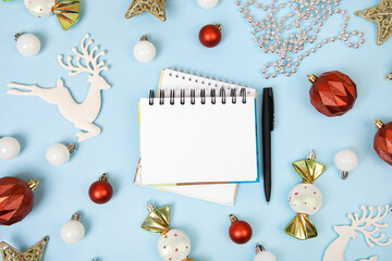 Christmas composition of golden stars and toys on Christmas tree, with open blank notebook and pen on blue background for writing goals and plans for the New Year. Flat lay, copy space