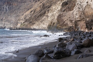 Dramatic Atlantic coast with black volcanic sand, waves splashing on rocks, and cliffs in Tenerife, Canary Islands. Natural coastal landscape with sea foam, volcanic textures, and wild ocean energy. © Olha