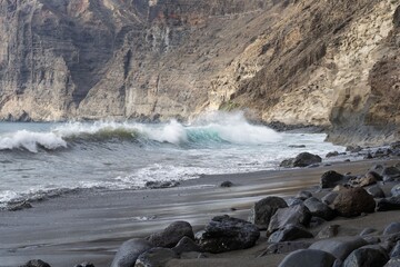 Dramatic Atlantic coast with black volcanic sand, waves splashing on rocks, and cliffs in Tenerife, Canary Islands. Natural coastal landscape with sea foam, volcanic textures, and wild ocean energy.
