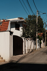 Narrow residential street with traditional houses, tiled roofs, and concrete fences under a clear blue sky