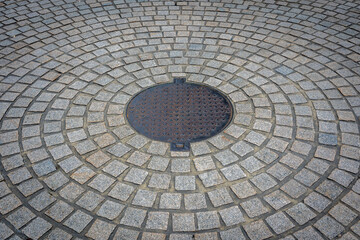 Circular cobblestone pavement with metal manhole cover in a radial pattern