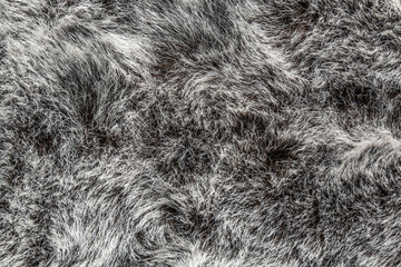 close-up view artificial fur featuring textured surface with soft, wavy fibers. colors range from deep black to light gray, creating an appealing pattern.