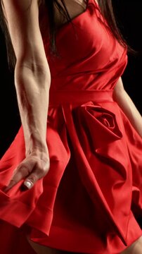 Stunning Black-Haired Woman in Ruby Red Dress and High Heels Gracefully Posing Against a Black Background, Captured in Super Slow Motion. Camera Rotation. Speed Ramp Effect. Vertical Aspect Ratio.