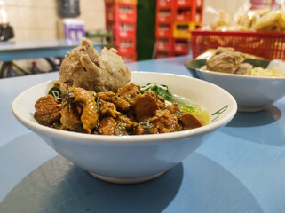 A bowl of chicken noodles with meatball tendons served in a white ceramic bowl. This Indonesian noodle dish is topped with soy sauce-seasoned chicken and meatball tendons and beef.