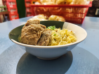 A bowl of chicken noodles with meatball tendons served in a white ceramic bowl. This Indonesian noodle dish is topped with soy sauce-seasoned chicken and meatball tendons and beef.