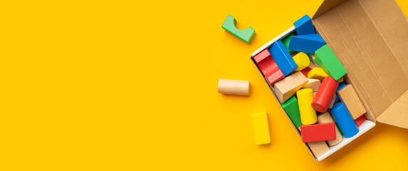 Wooden children's multi-colored bright construction set blocks in cardboard box on yellow...