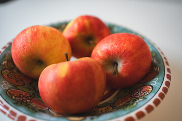 Four red apples rest beautifully in a decorative ceramic bowl. Their shiny skin reflects light, showing off vibrant tones of red and yellow. 
