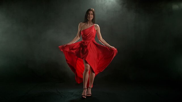 Stunning Black-Haired Woman in Ruby Red Dress and High Heels Gracefully Posing Against a Black Background, Captured in Super Slow Motion for a Dramatic and Elegant Fashion Cinematic Effect.