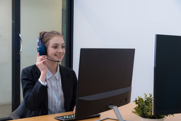 Young woman with headset smiles while working at desk in modern office environment. She appears engaged and professional, showcasing positive attitude in her role.