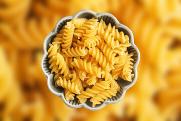 Dry fusilli pasta in decorative bowl. Yellow macaroni texture background. Italian cuisine concept....