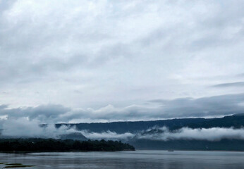 Misty Mountain Scene with Floating Clouds and Serene Water Reflection