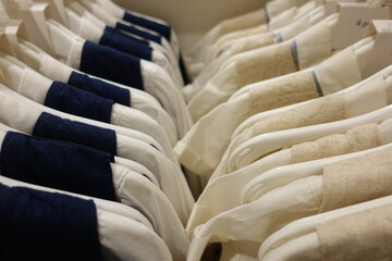 Soft pastel pink blue yellow cream baby clothes neatly arranged on white plastic hangers in a boutique store, highlighting delicate embroidery and gentle cotton texture for newborn girls.