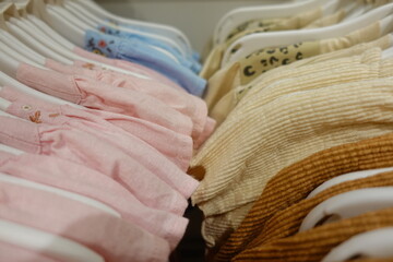 Soft pastel pink blue yellow cream baby clothes neatly arranged on white plastic hangers in a boutique store, highlighting delicate embroidery and gentle cotton texture for newborn girls.