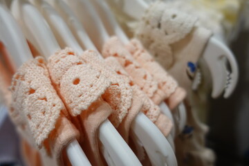 Soft pastel pink blue yellow cream baby clothes neatly arranged on white plastic hangers in a boutique store, highlighting delicate embroidery and gentle cotton texture for newborn girls.