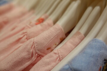 Soft pastel pink blue yellow cream baby clothes neatly arranged on white plastic hangers in a boutique store, highlighting delicate embroidery and gentle cotton texture for newborn girls.