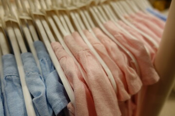 Soft pastel pink blue yellow cream baby clothes neatly arranged on white plastic hangers in a boutique store, highlighting delicate embroidery and gentle cotton texture for newborn girls.